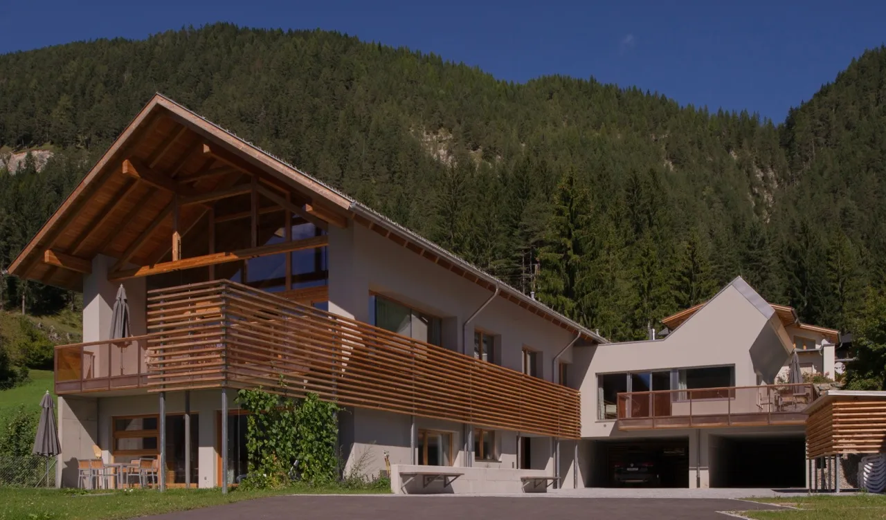 Wohnbau mit Holzfassade vor bewaldetem Hang